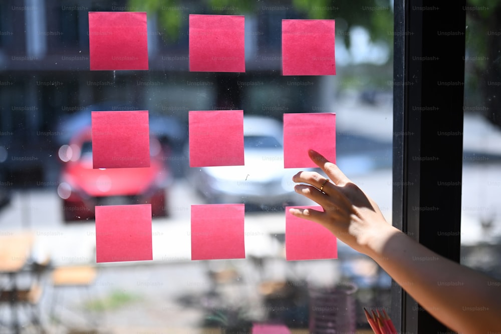 Cropped shot of businesswoman reading sticky notes on glass wall office.