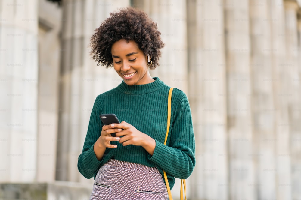 Portrait d’une femme d’affaires afro utilisant son téléphone portable tout en se tenant à l’extérieur dans la rue. Concept d’entreprise et urbain.