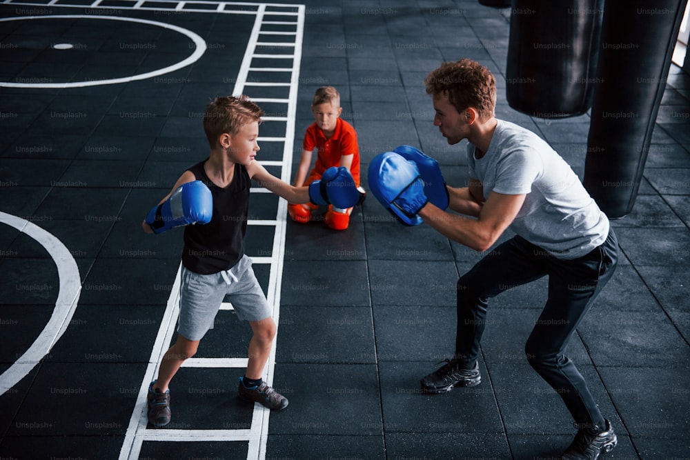 Young trainer teaches kids boxing sport in the gym.