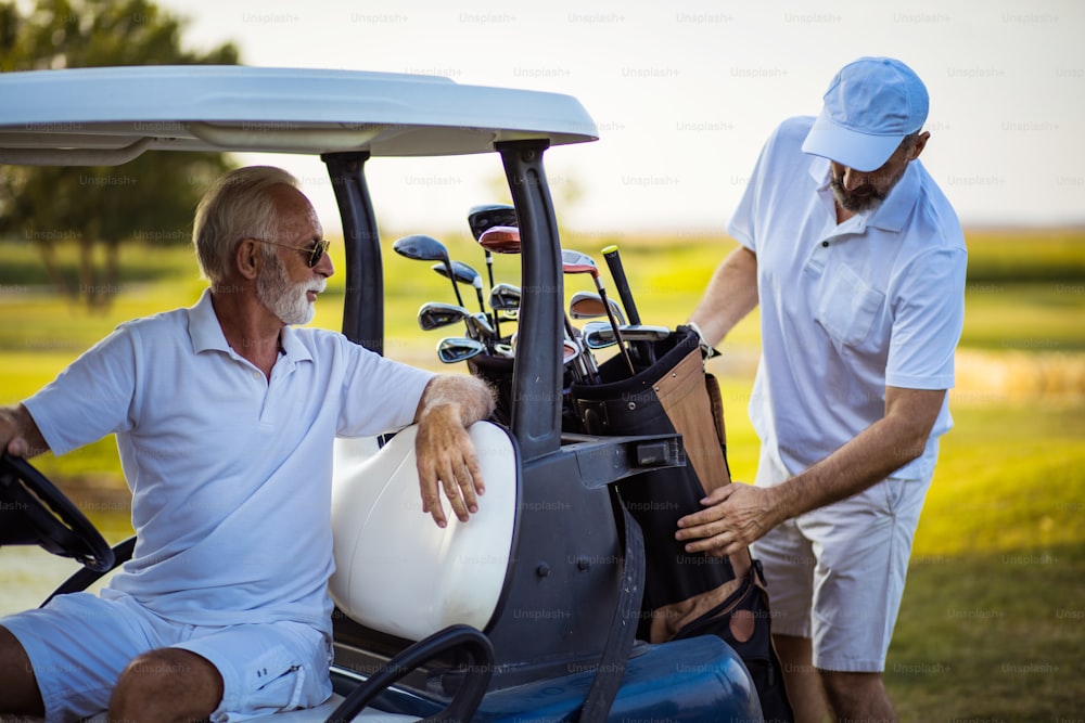 Due golfisti uomini anziani in campo. Uomo seduto in carrello da golf.