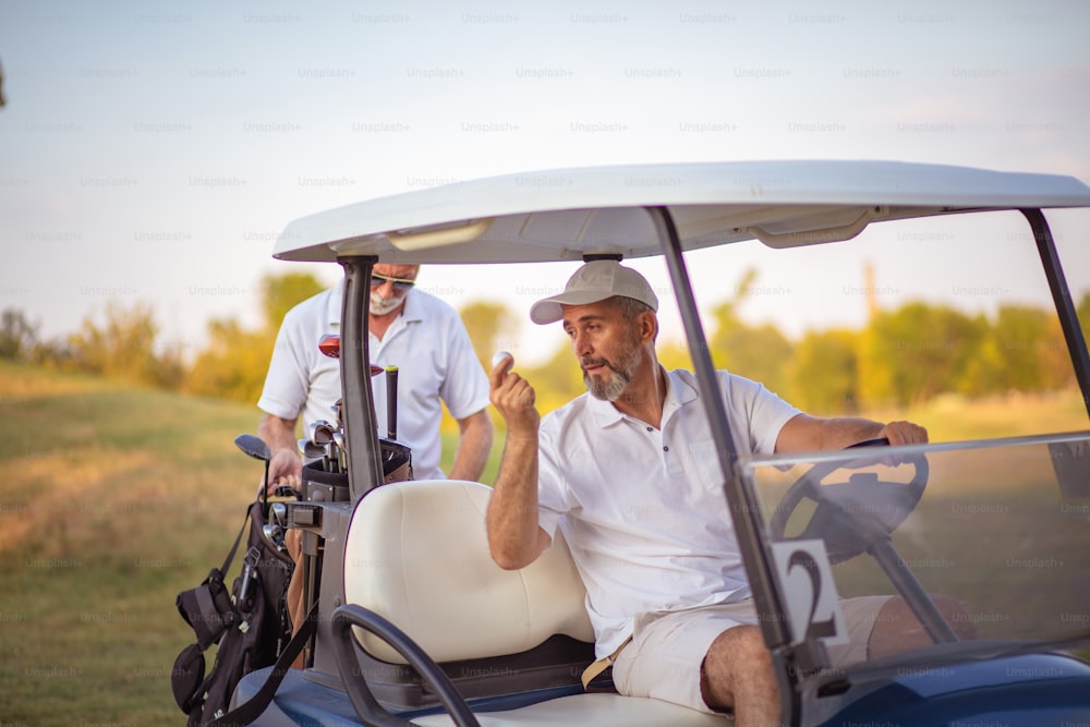 Dos golfistas senior en la cancha. Hombre sentado en carrito de golf.