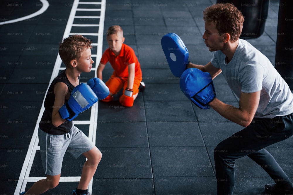 Young trainer teaches kids boxing sport in the gym.
