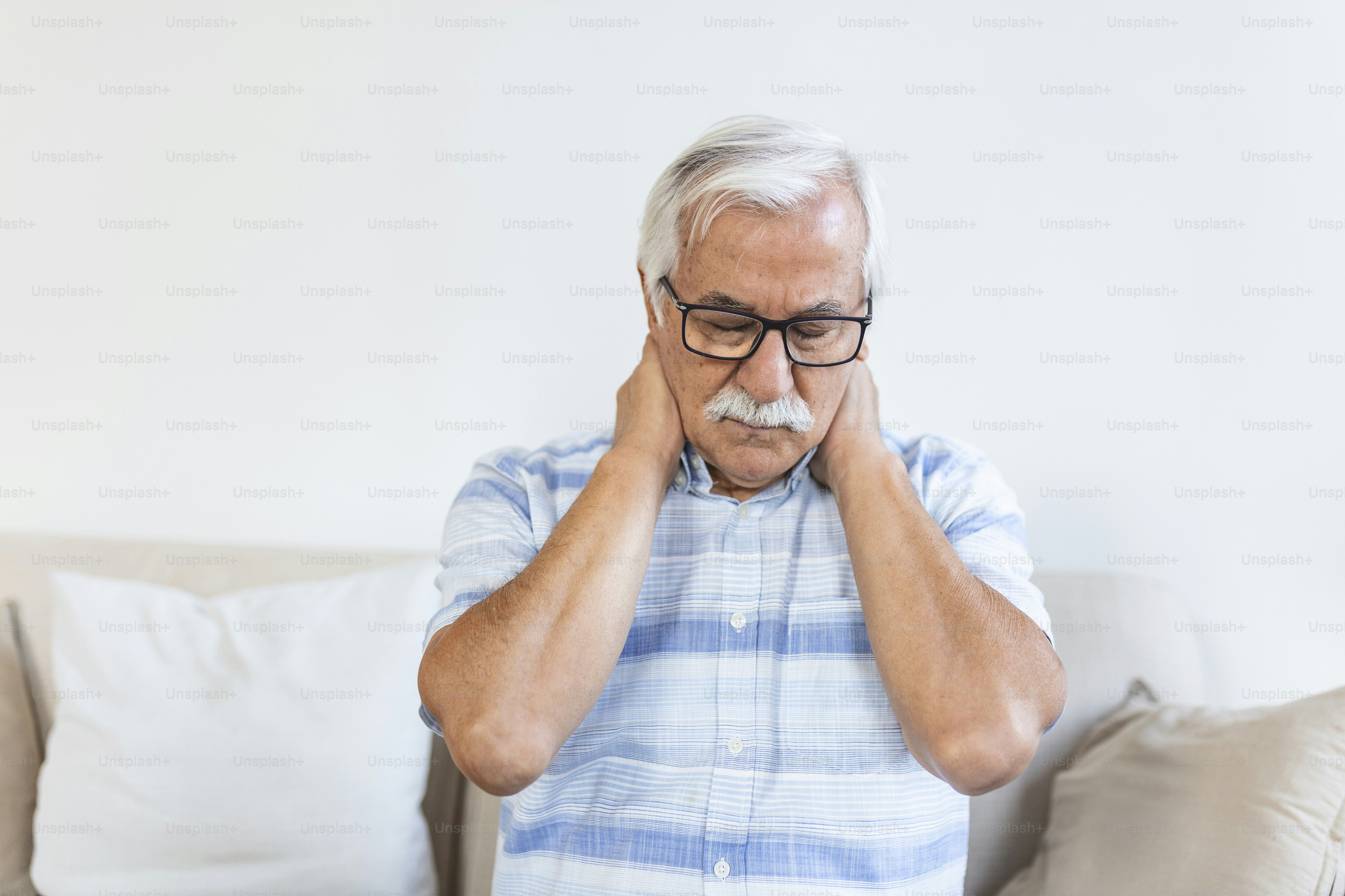 Un homme plus âgé à la moustache blanche, portant des lunettes, se tenant le cou de douleur