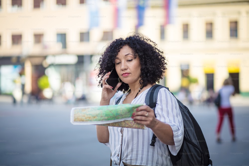 Woman standing on street with map in hands and talking on phone.