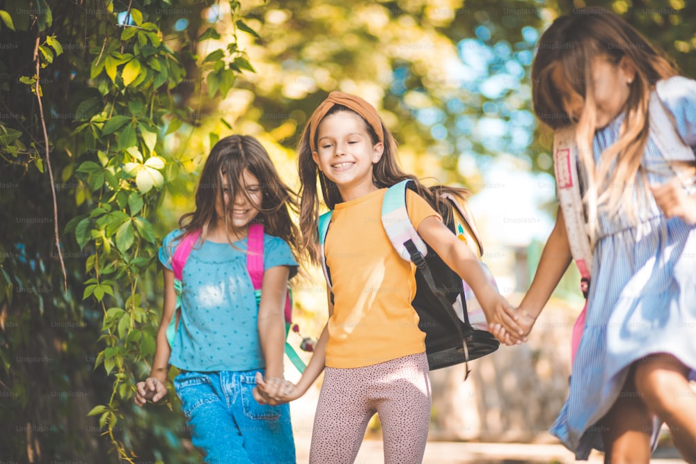 Basta scuola per oggi. Tre bambine che corrono attraverso la natura con lo zaino di scuola sul retro.
