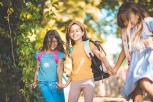 Suficiente escuela por hoy. Tres niñas pequeñas corriendo por la naturaleza con la mochila escolar en la espalda.