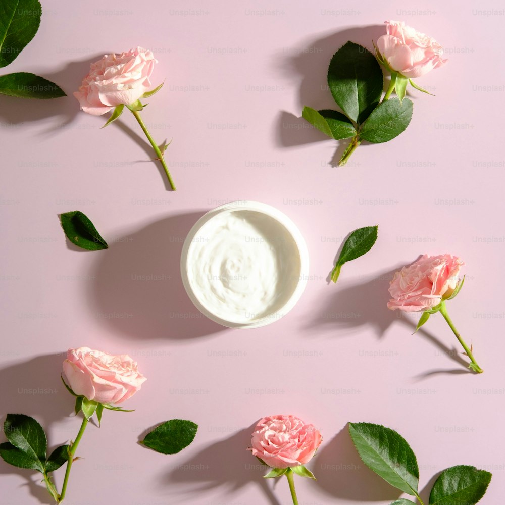 Tarro de crema hidratante y flores de rosa sobre fondo rosa. Concepto cosmético de rosas SPA.
