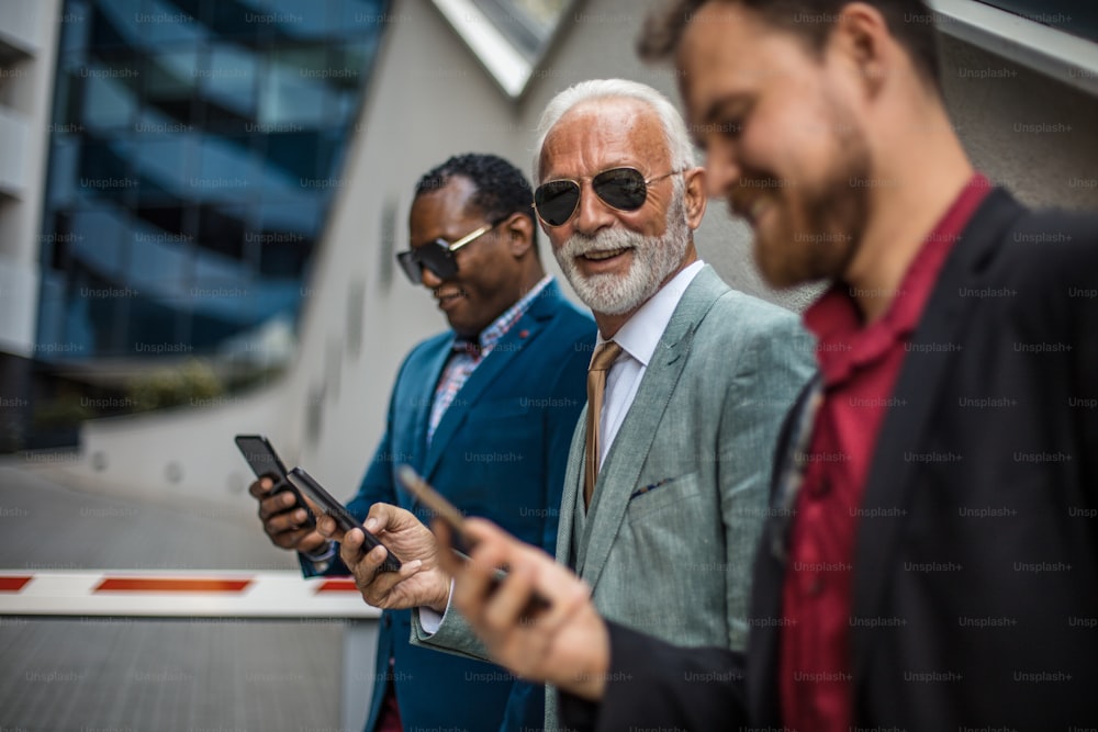 Three business men in the city standing on street and using mobile phones.  Focus is on background.
