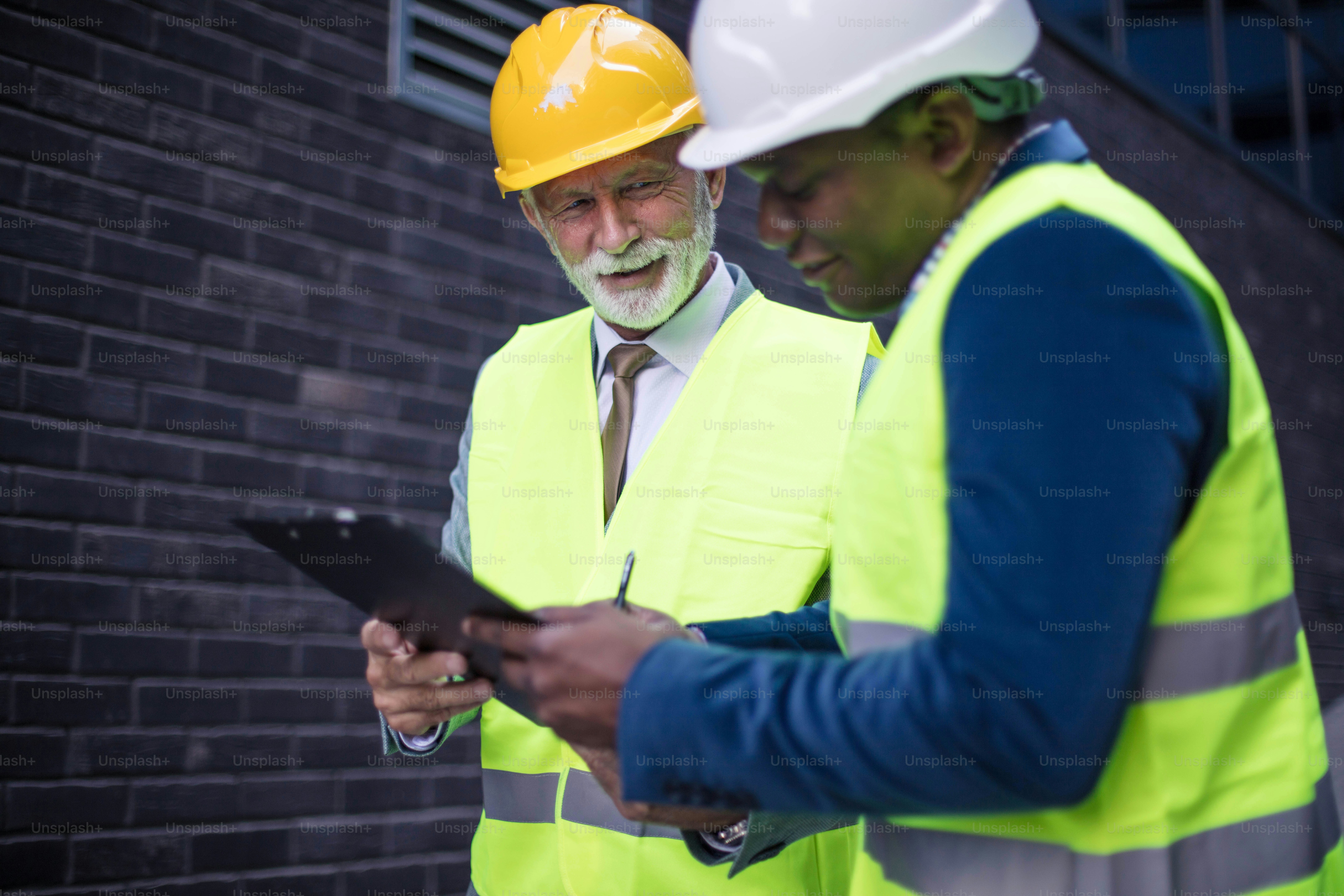Reifer Ingenieur bespricht die Struktur des Gebäudes mit Architektenkollegen auf der Baustelle. Dokument signieren.