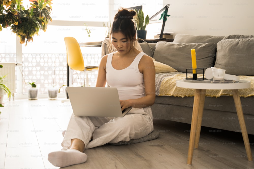 Full length view of girl freelancer sitting at the floor while working at computer from home. Lockdown, isolation, quarantine, remote, distant business online education concept