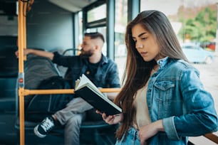 Mujer joven hermosa leyendo un libro mientras está de pie en un autobús en movimiento