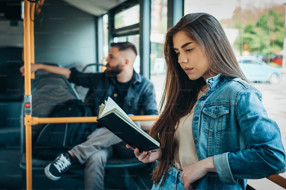 Young beautiful woman reading a book while standing in a moving bus