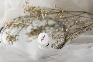 Bague ronde blanche moderne élégante et fleurs séchées sur miroir sur tulle blanc doux, espace de copie. Bague en verre fusionné à la mode inhabituelle. Cadeau contemporain