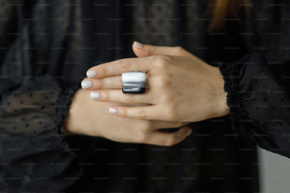 Beautiful stylish woman with modern square black and white ring on hand and white manicure, closeup. Fashionable female in black dress with unusual fused glass accessory. Beauty and care.