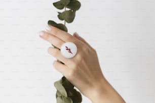 Elegante anillo redondo blanco moderno en hermosa mano con rama de eucalipto sobre fondo blanco. Anillo de vidrio fundido de moda inusual en la mano femenina con manicura blanca. Concepto ecológico y de cuidado