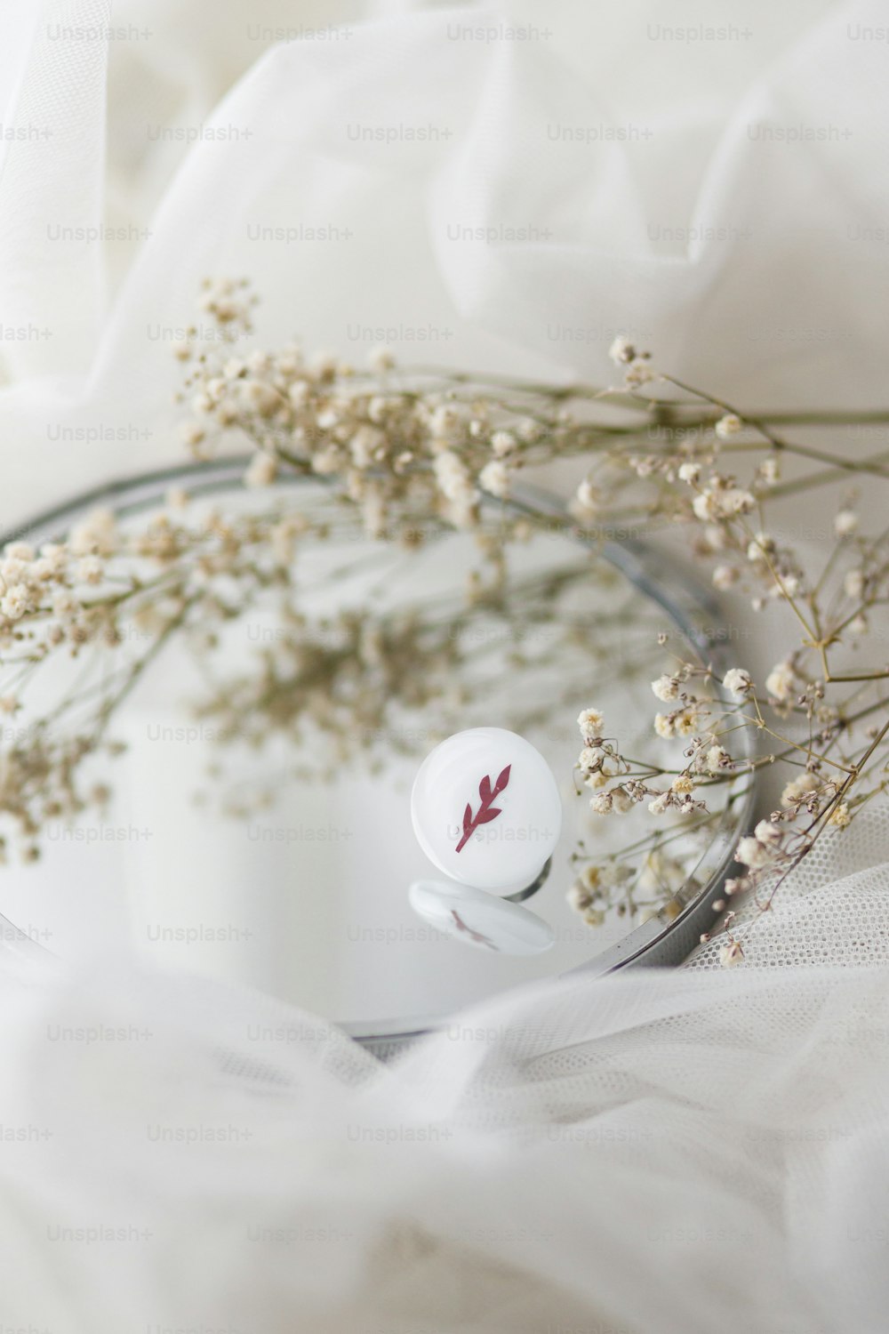 Stylish modern white round ring and dried flowers on mirror on soft white tulle, copy space. Unusual fashionable fused glass ring. Contemporary gift