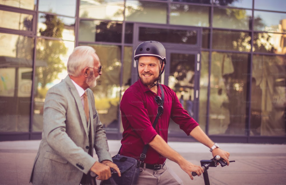 Talking about work.  Two business men riding electric scooter in the city.