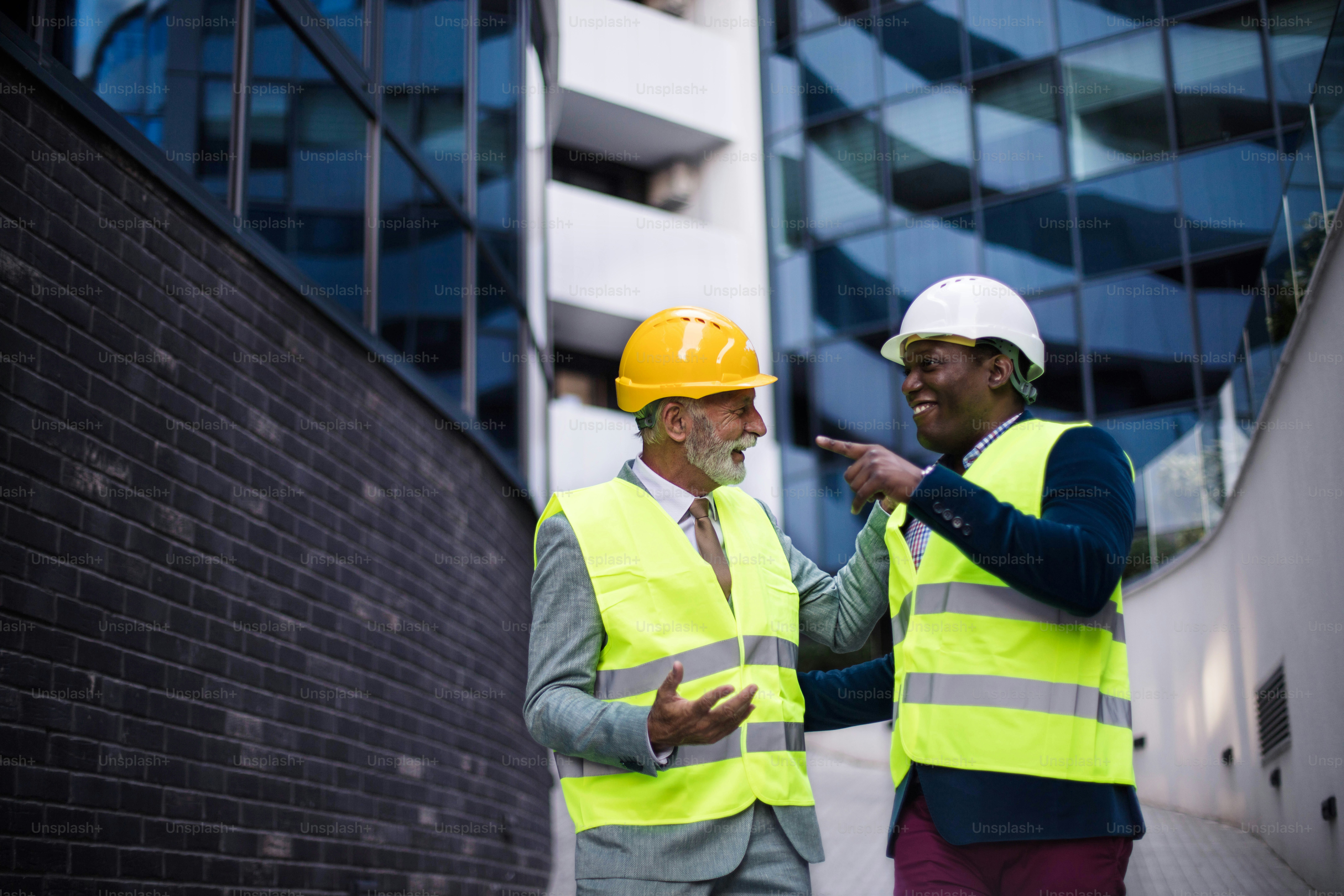 Mature engineer discussing the structure of the building with architects colleague at construction site. Businessmen talking