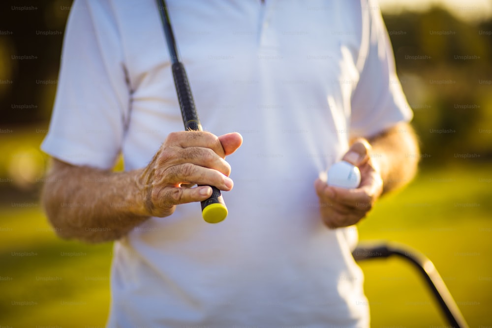 Senior golfer on court holding ball. Focus is on hand.