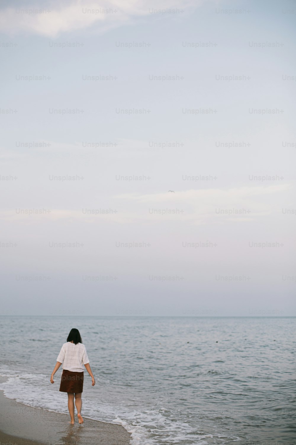 Carefree hipster woman walking barefoot on sandy beach with sea waves in the evening, enjoying tranquil moment. Casual young female  relaxing on seashore at resort. Mindfulness