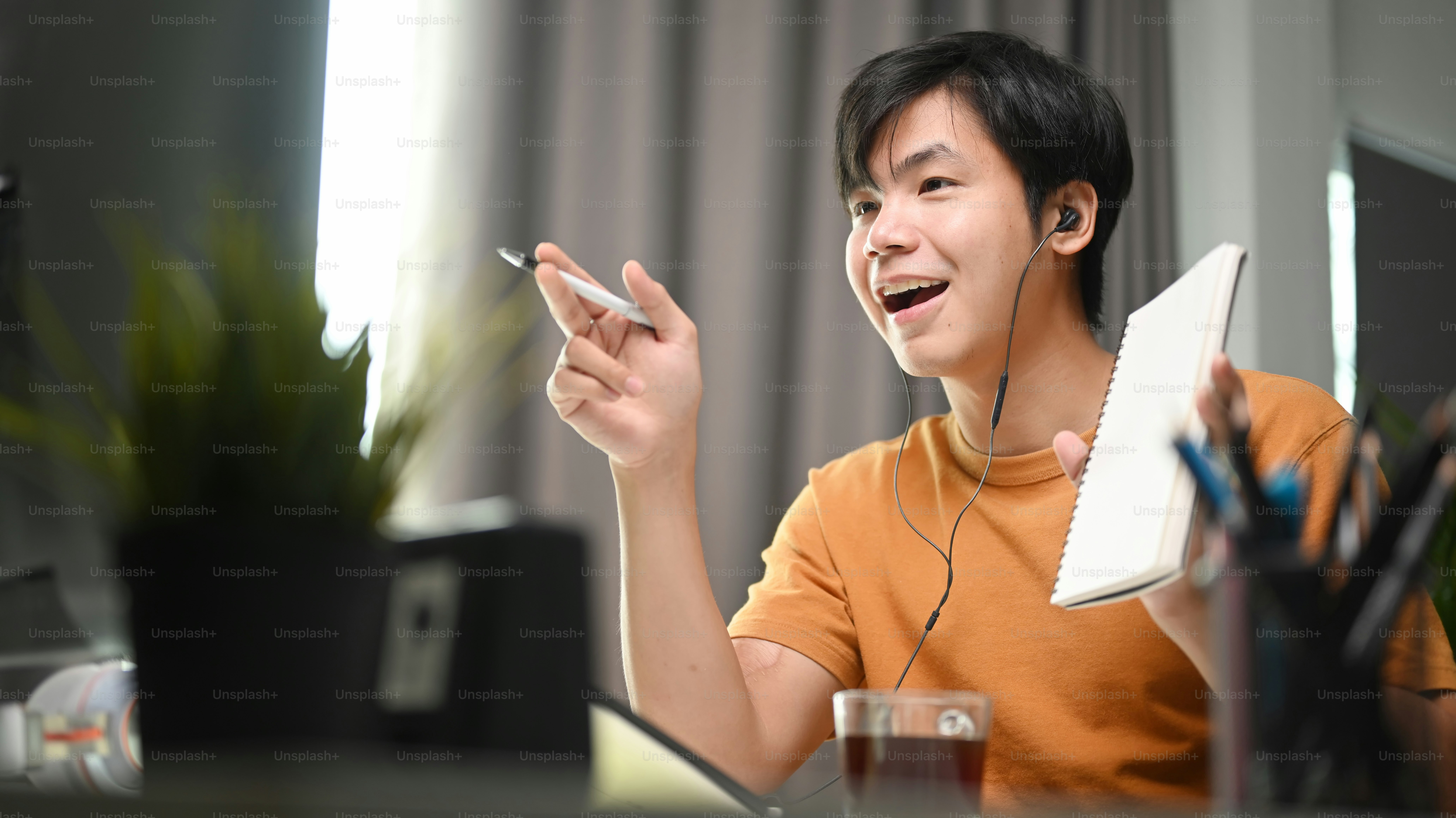 Pria muda dengan earphone melakukan konferensi video selama bekerja online dari rumah.