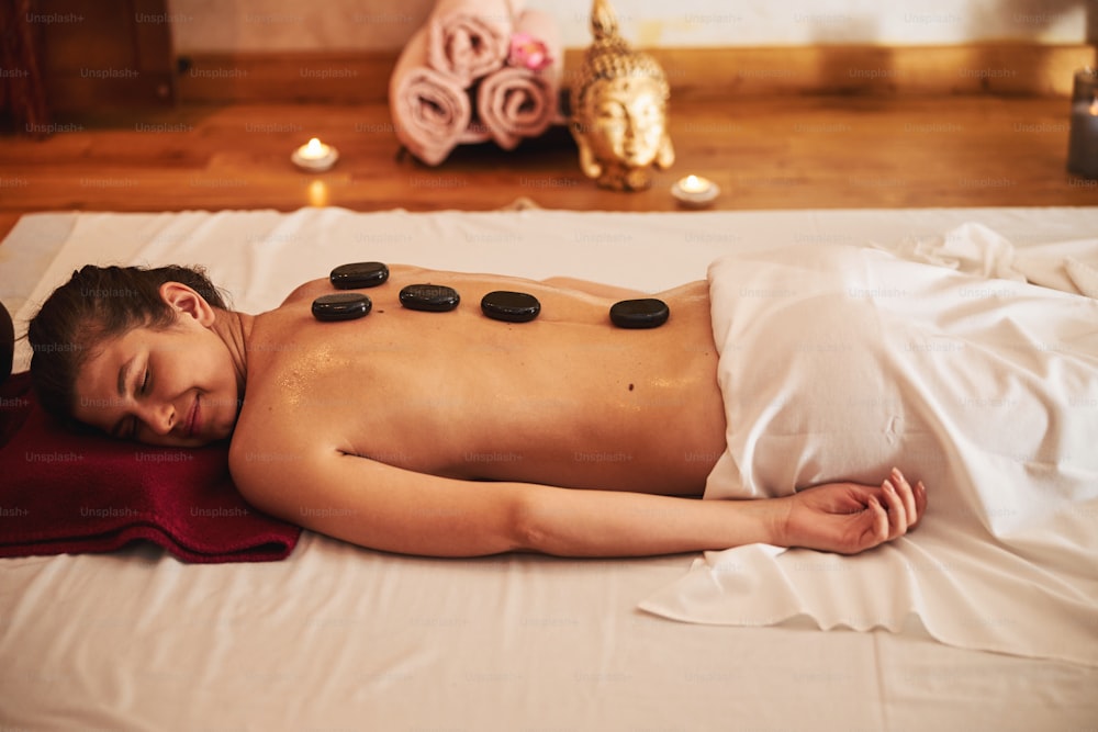 Female lying with comfort on white mattress while having massage stones distributed on her back