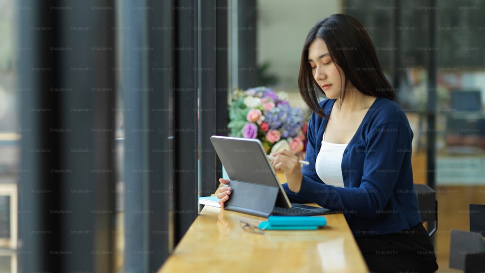 Portrait of female teenager using digital tablet with stylus and keyboard in coffee shop