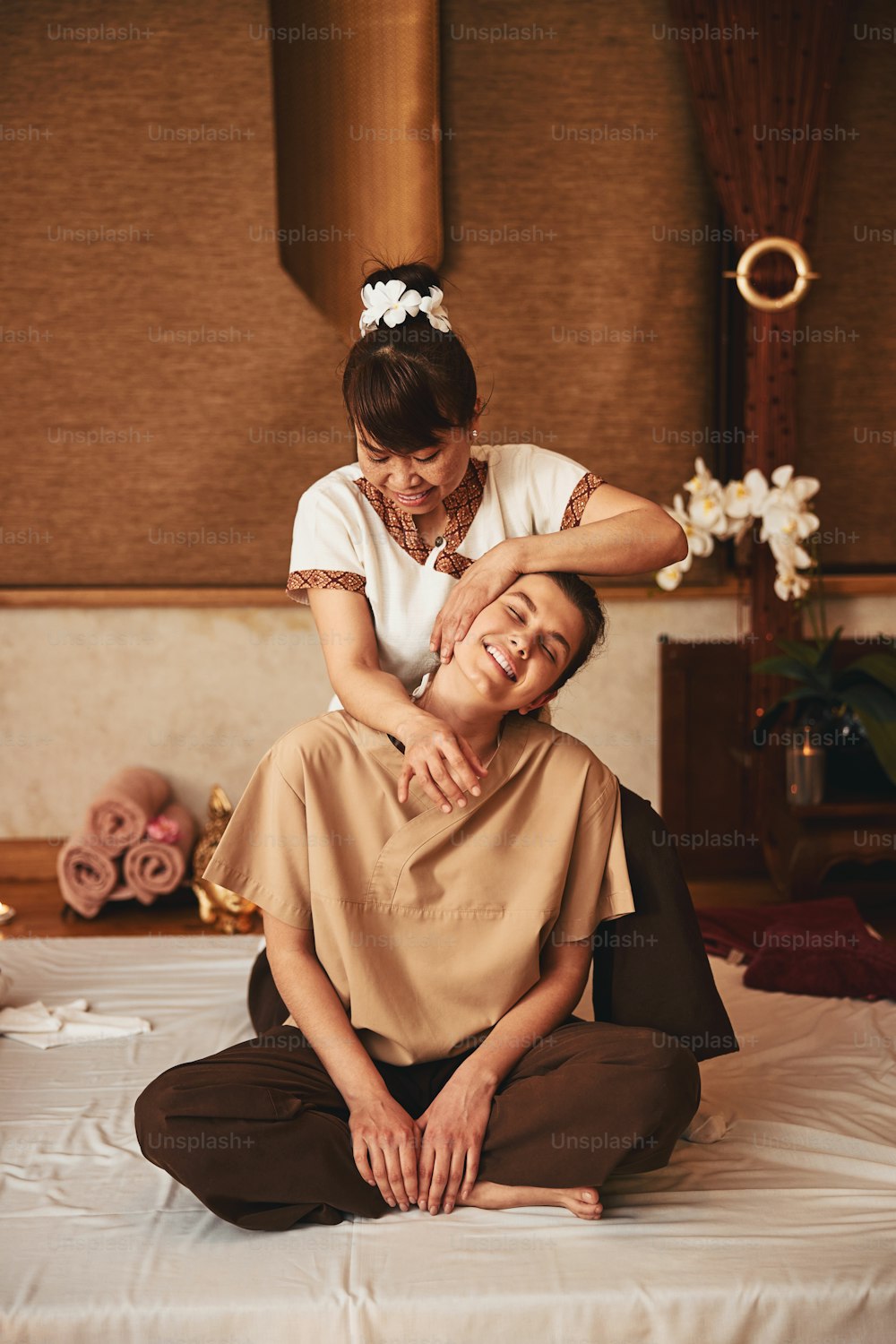 Thai massage salon worker tilting head of relaxed female to left while laying hand on her ear