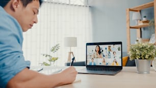 Young Asia businessman using laptop talk to colleagues about plan in video call meeting while work from home at living room. Self-isolation, social distancing, quarantine for corona virus prevention.