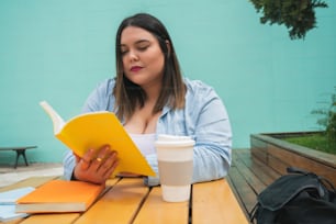 Porträt einer jungen Plus-Size-Frau, die Freizeit genießt und ein Buch liest, während sie draußen im Café sitzt.