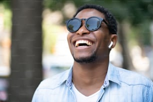 Homme afro-américain portant des lunettes de soleil et souriant tout en marchant à l’extérieur dans la rue. Concept urbain.