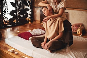 Woman keeping herself in lotus pose while Thai massage therapist, standing behind, leaning her head to right side