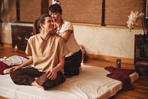 Fürsorgliche Thai-Massage-Expertin, die linke Handfläche unter dem Kinn der Klientin hält, die rechte Hand auf ihrem Nacken hält und ihren Kopf dreht