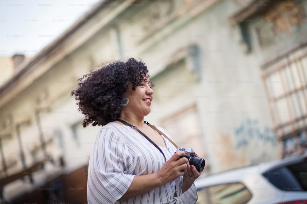 She is a city girl.  Smiling woman with camera on the street.