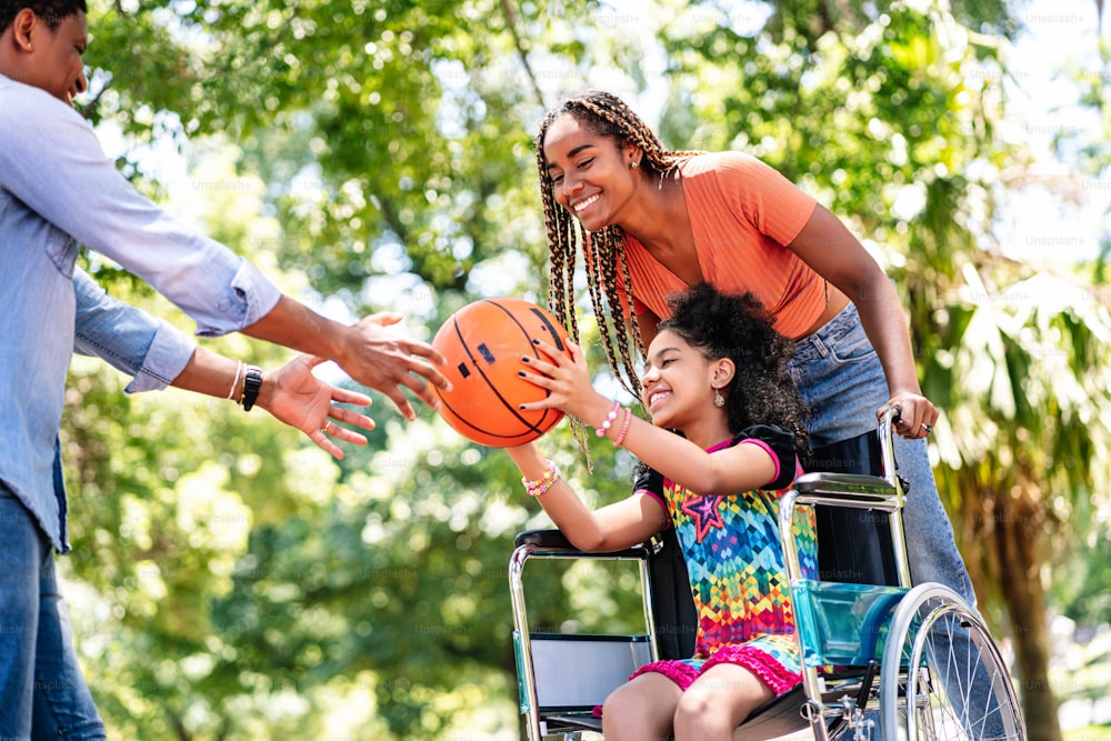 Little girl in a wheelchair enjoying and playing basketball with her family at the park.