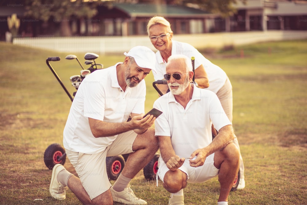 Golfistas seniores em quadra. Dois homens usando o telefone inteligente.