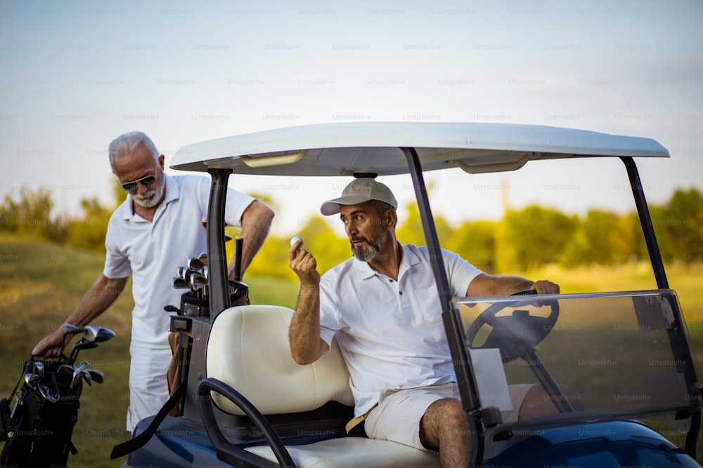 Two senior men golfers on court. Man sitting in golf cart.