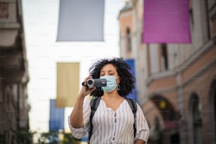 Femme en train d’enregistrer.  Femme filmant dans la rue et portant un masque de protection.