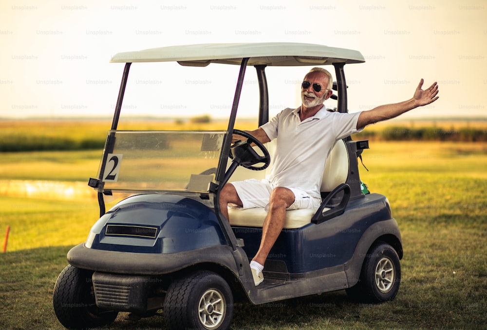 Senior man driving golf car and waving.