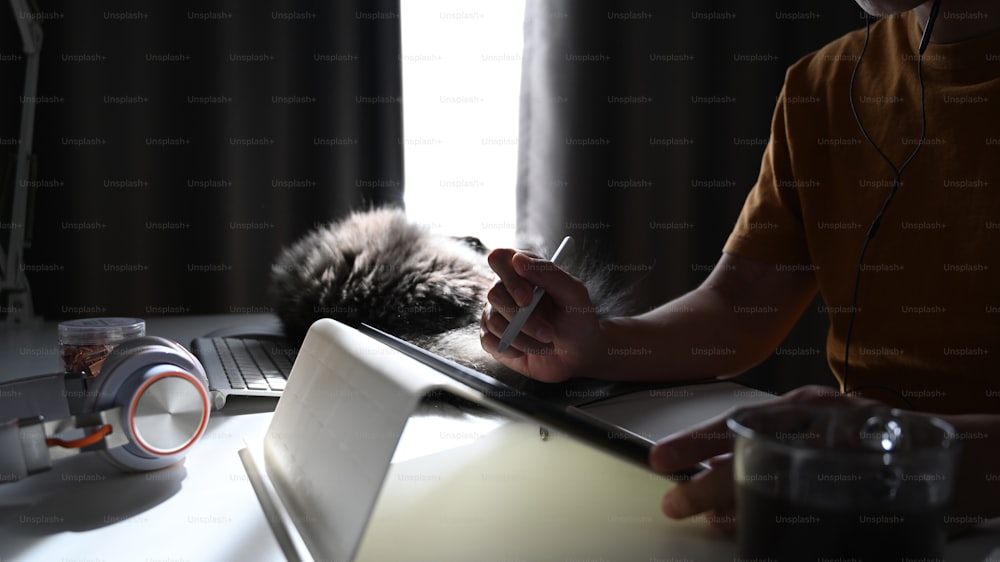 거실에서 고양이와 함께 앉아 디지털 태블릿으로 작업하는 남자의 잘린 사진.