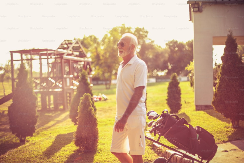 ゴルフバッグを持って歩く年配の男性。
