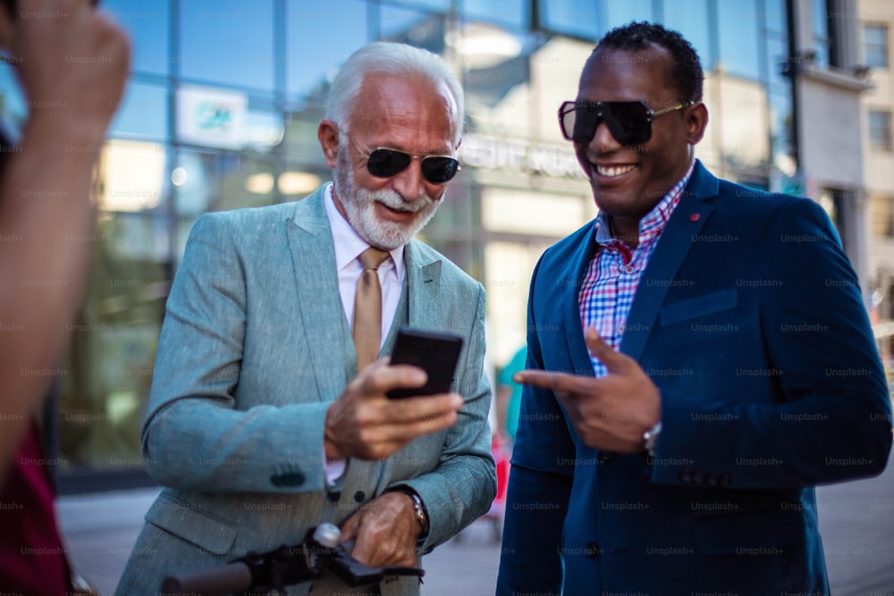 Business colleagues using mobile phone outdoors in city. Focus is on men.