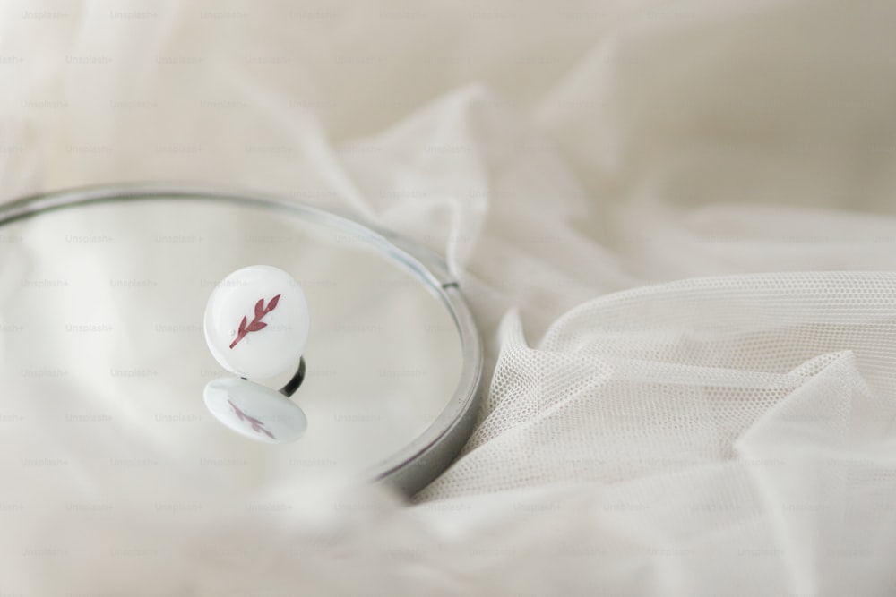 Stylish modern white round ring on mirror on soft white tulle, copy space. Unusual fashionable fused glass ring. Contemporary gift