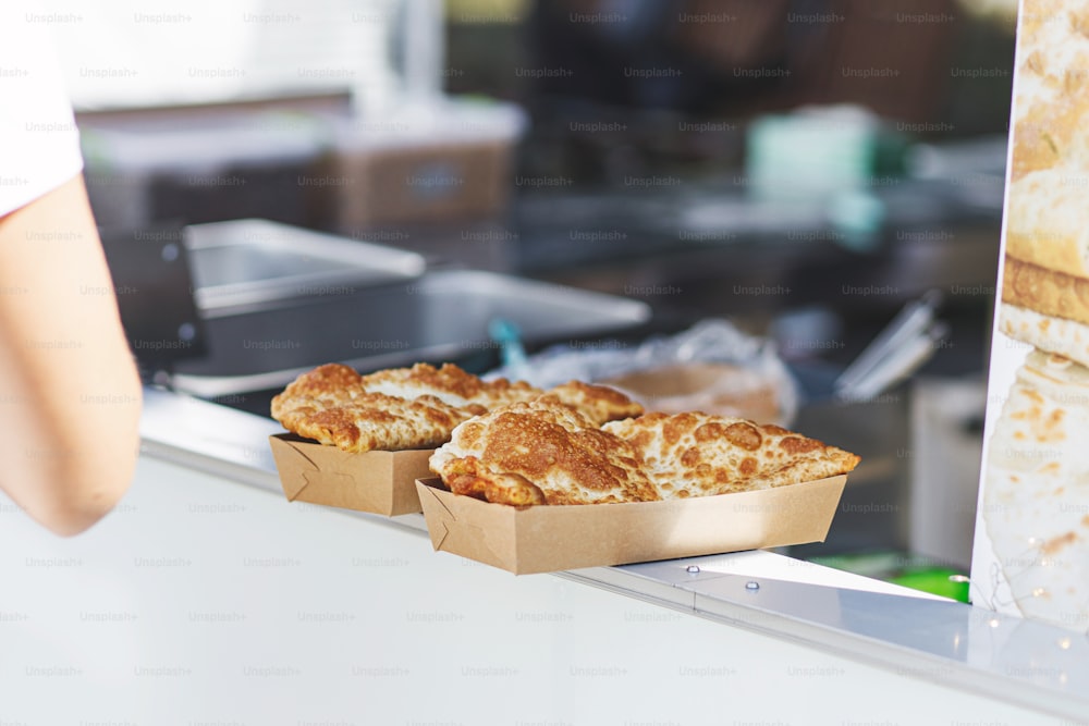 Delicious fried cheburek in takeaway box, cooking traditional pie with meat at street food festival. Baked bun stuffed with beef meat. Street food to go. Summer picnic