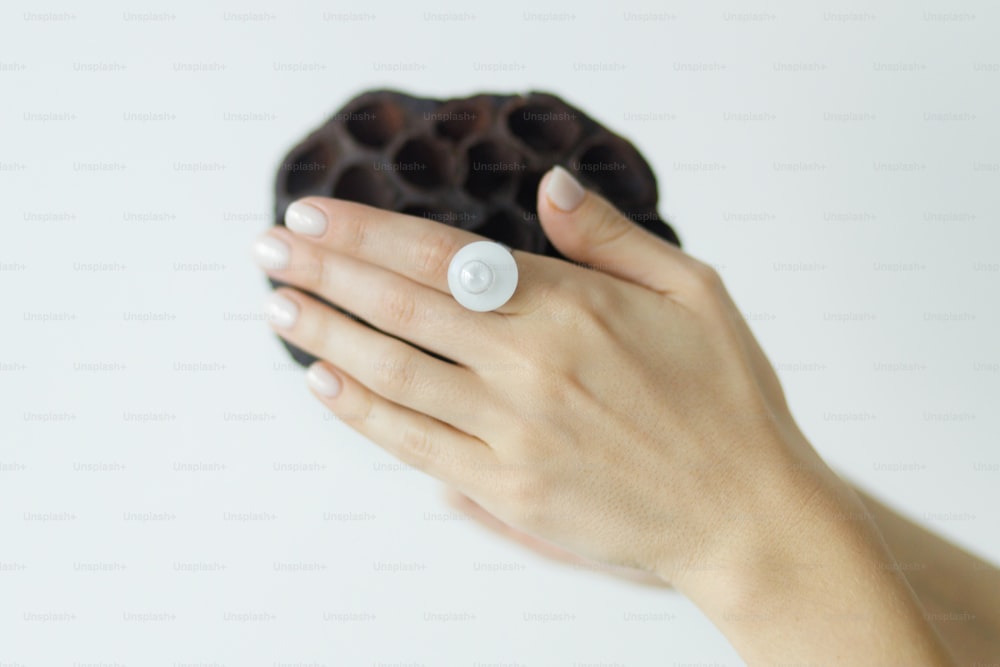 Stylish modern white round ring on beautiful hand with dried lotus on white background. Unusual fashionable fused glass ring on female hand with white manicure. Eco and care concept