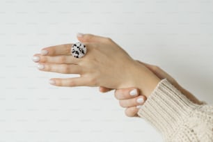 Elegante anillo redondo moderno blanco y marrón en hermosa mano sobre fondo blanco. Anillo de vidrio fundido de moda inusual en la mano femenina con manicura blanca. Regalo contemporáneo