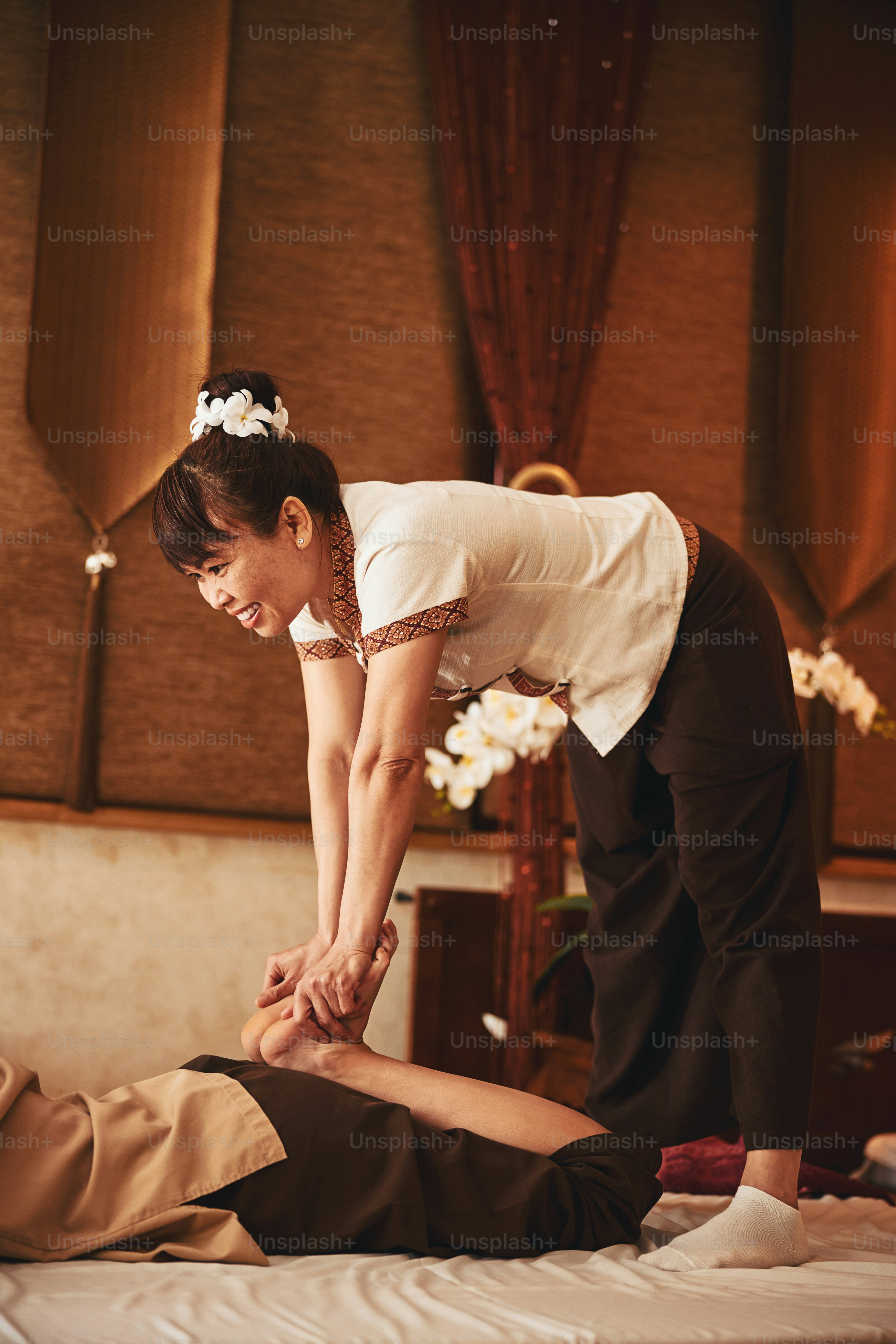Terapis pijat yang menyenangkan berdiri dengan kaki selebar bahu dan membungkuk ke depan sambil menggosok dan menekan kaki pengunjung