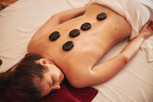 Five smooth warm stones on bare back of female in massage parlour during muscles treatment procedure