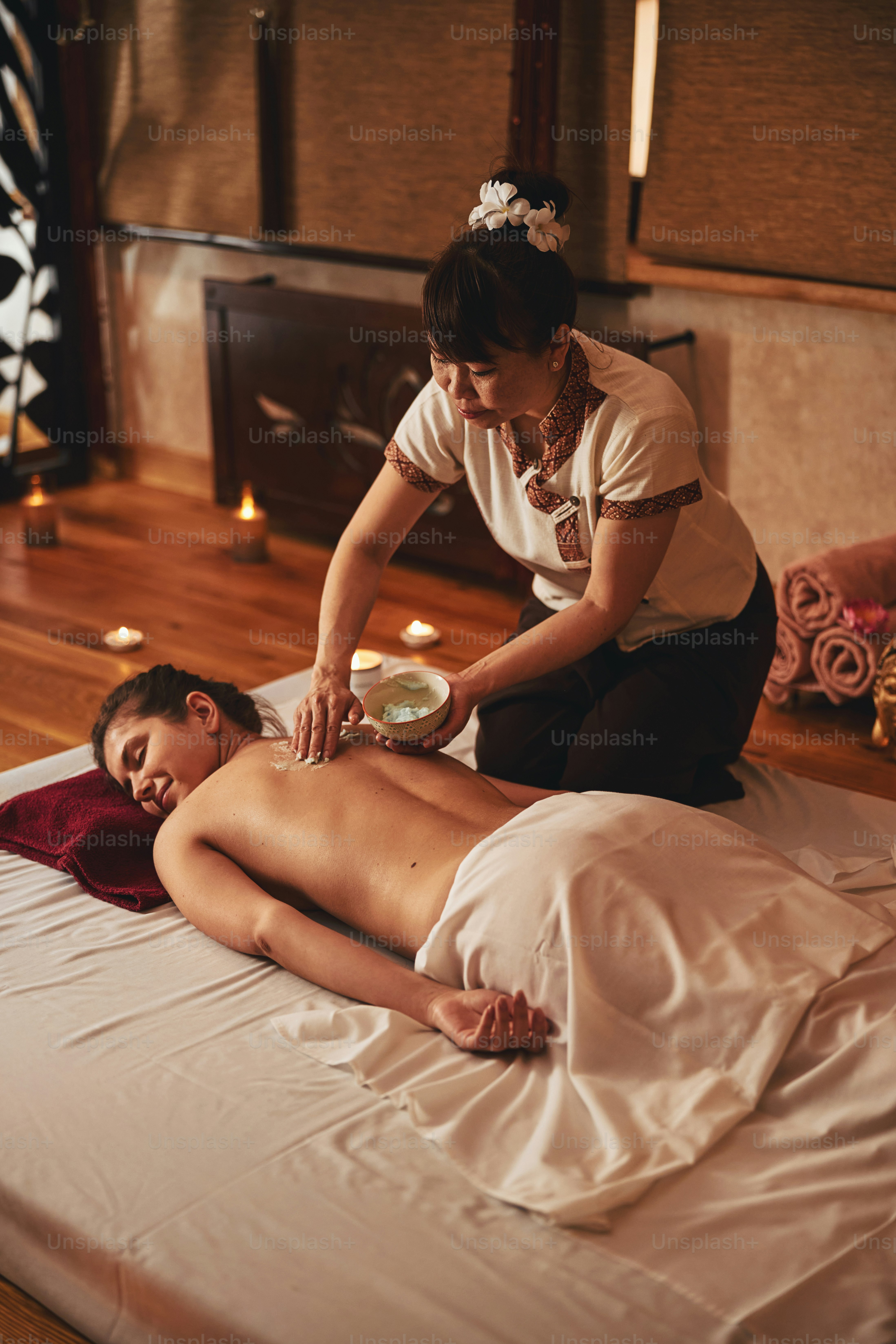 Belakang wanita yang sedang beristirahat ditutupi dengan balsem hijau organik dari mangkuk dengan tangan pakar kecantikan Asia