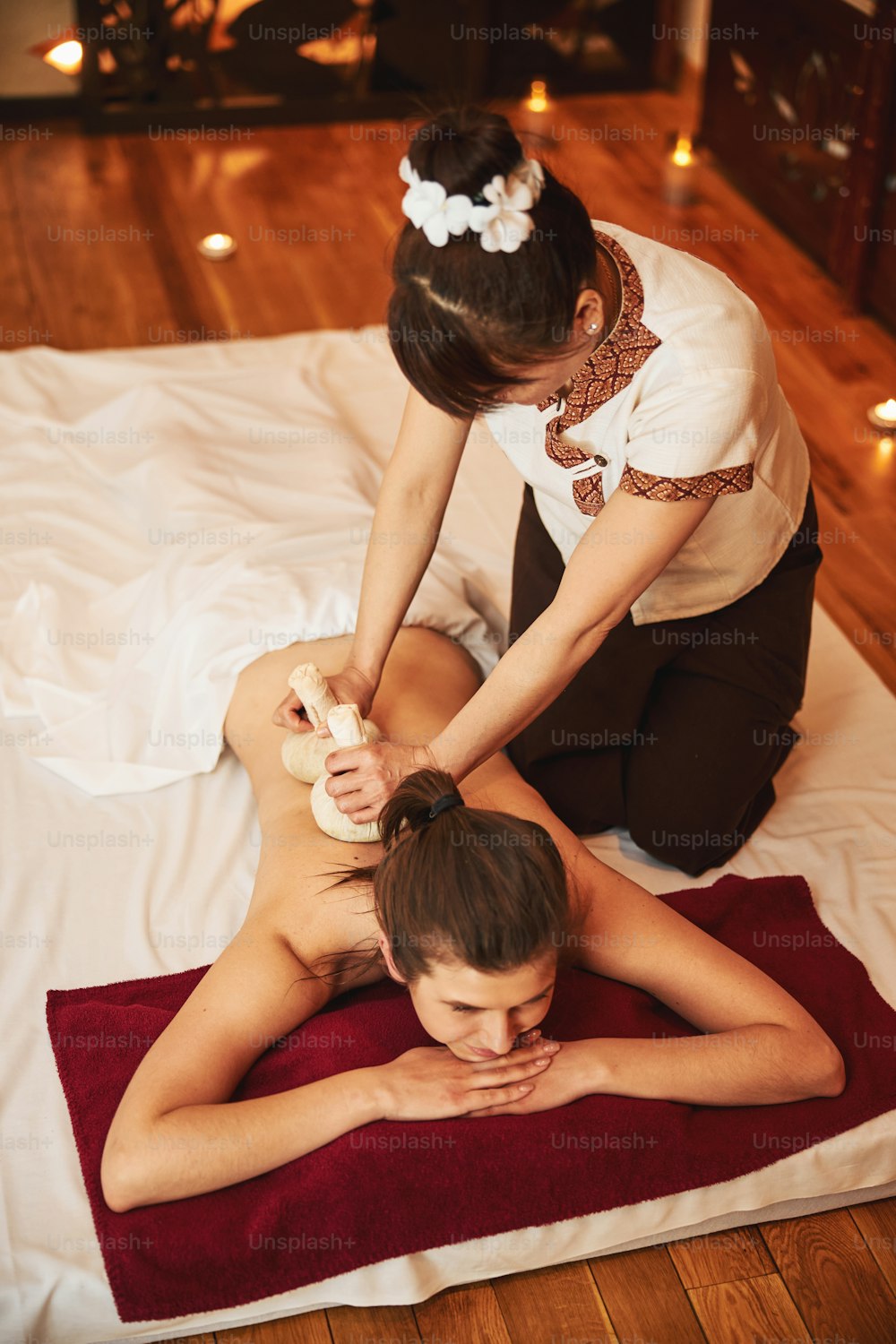 Massage specialist performing thai massage by putting a pair of herbal balls on back of female in prone position